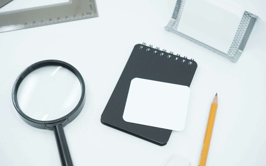 Notebook, pencil and magnifying glass arranged on a clean white desk